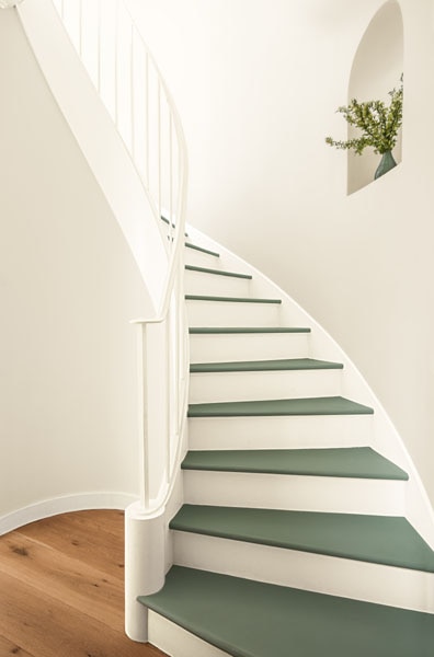 A curved stairway with walls painted in Sea Salt CSP-95 and stair treads painted in Rosepine 461. A floral arrangement decorates the curved alcove.