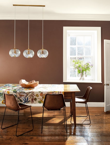 A dining room with three glass pendant lights hanging over a table decorated with a floral cloth. Colours are Leather Saddle Brown 2100-20 and Glacier White OC-37.