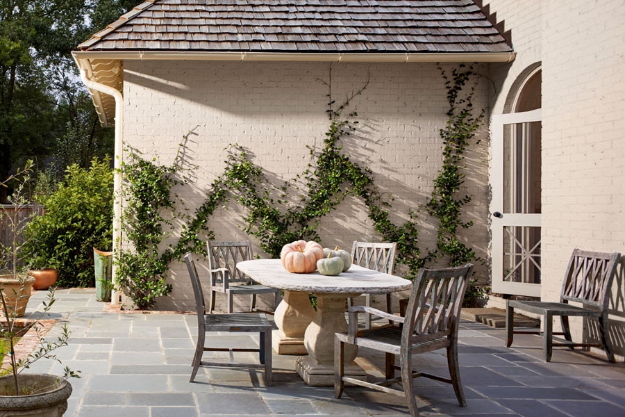 A patio scene with wooden table and chairs decorated with pumpkins.  The brick walls of the property are painted in Aura Exterior Low Lustre Evening White OC-81