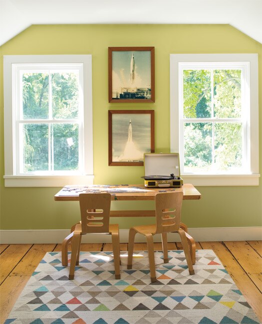 A contemporary study with walls painted in Green Hydrangea CSP-850. A colourful triangle-patterned rug and desk with 2 chairs, styled with a puzzle and record player, complete the look