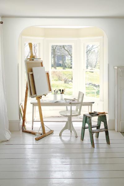 An artist's easle and work bench in front of a bay patio window.  The front walls are painted in Paper White OC-55 and the rear bay wall is painted in Ballet White OC-9